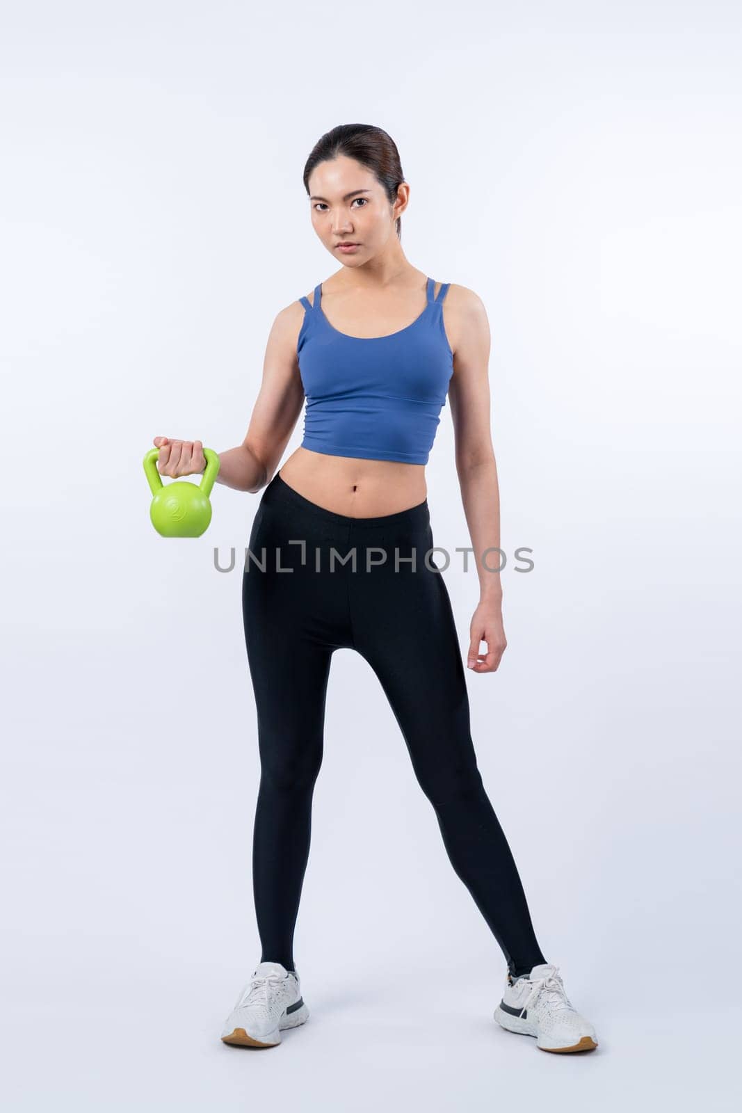 Vigorous energetic woman doing kettlebell weight lifting exercise on isolated background. Young athletic asian woman strength and endurance training session as body workout routine.