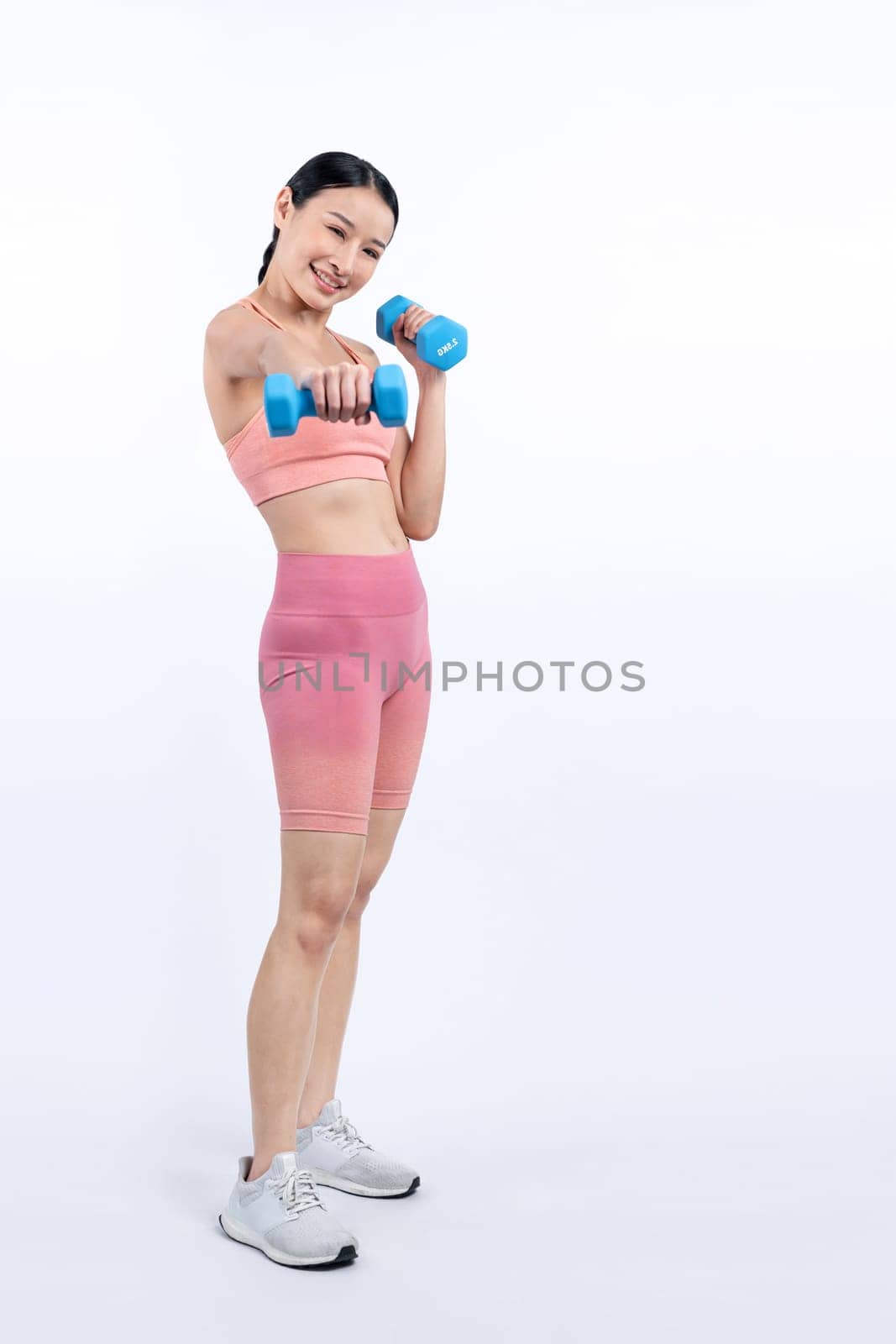 Vigorous energetic woman doing dumbbell weight lifting exercise on isolated background. Young athletic asian woman strength and endurance training session as body workout routine.