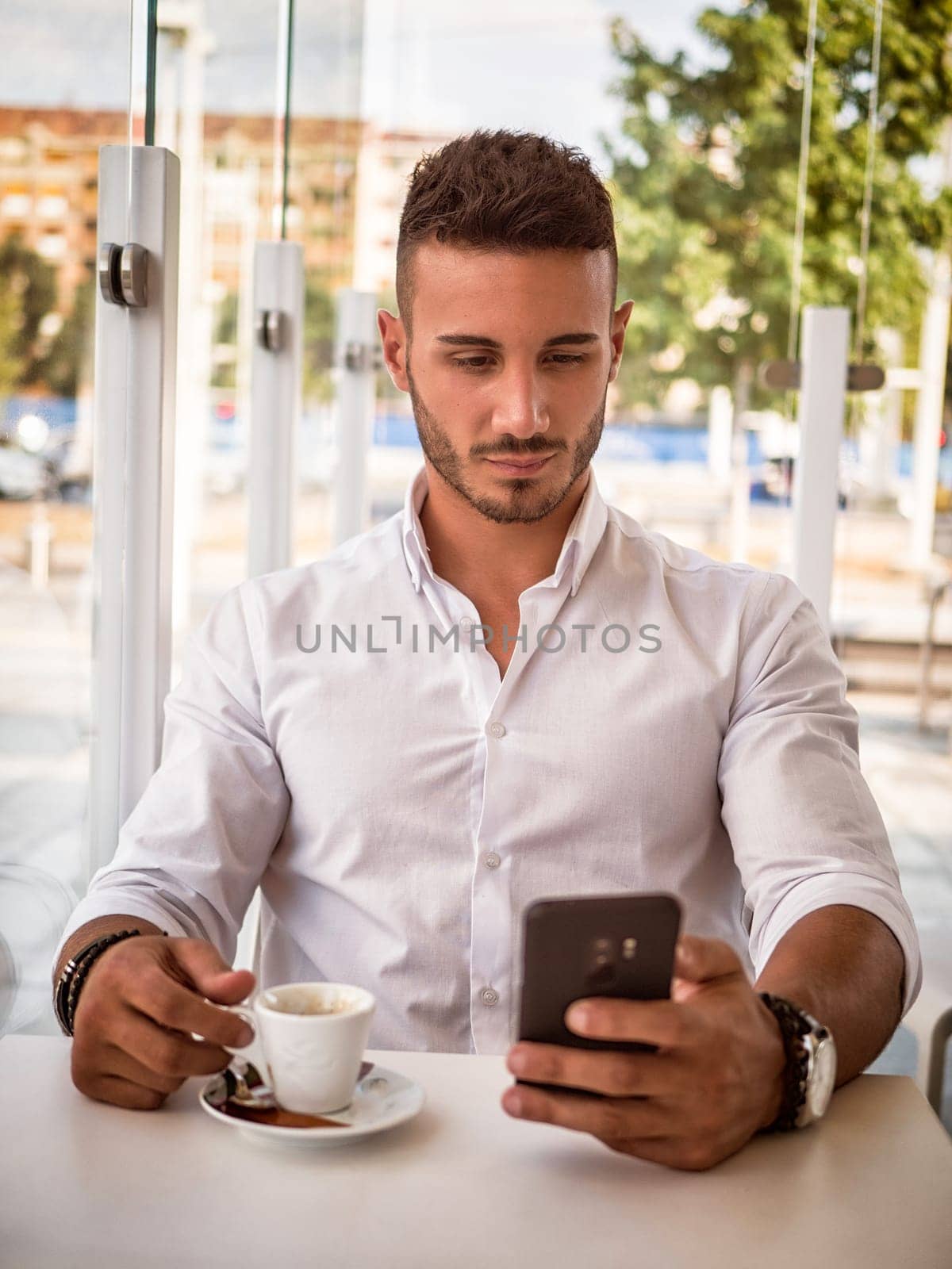 Photo of a young, handsome man engrossed in his cell phone at a table by artofphoto