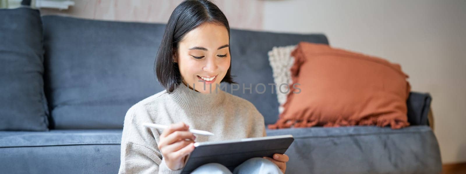 Creative young woman sitting with tablet and pen, drawing on digital application.