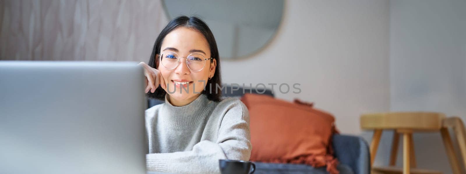 Beautiful asian girl works from home, studying with laptop, sitting in living room, being on remote, freelancing online.
