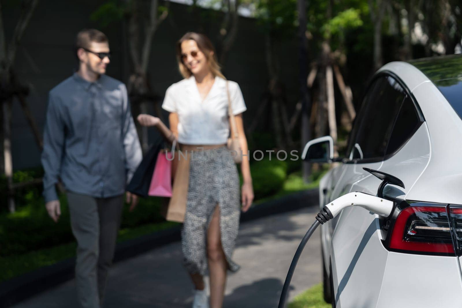 Young couple travel with EV electric car in green sustainable city innards by biancoblue