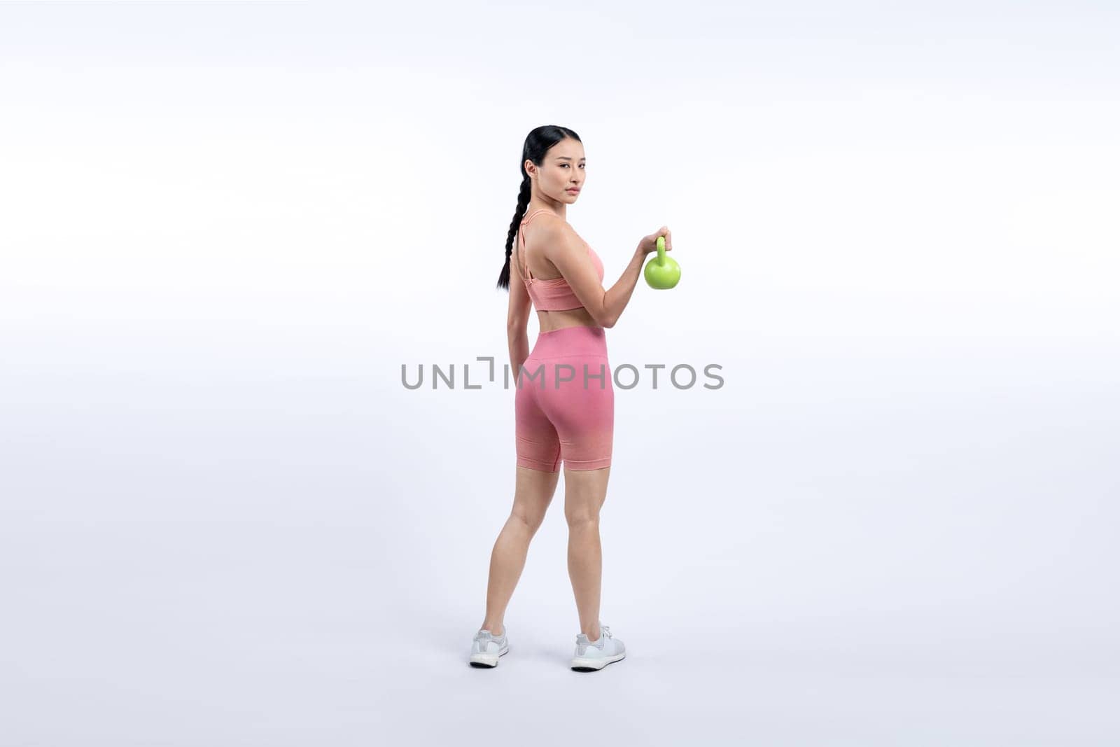 Vigorous energetic woman doing kettlebell weight lifting exercise on isolated background. Young athletic asian woman strength and endurance training session as body workout routine.