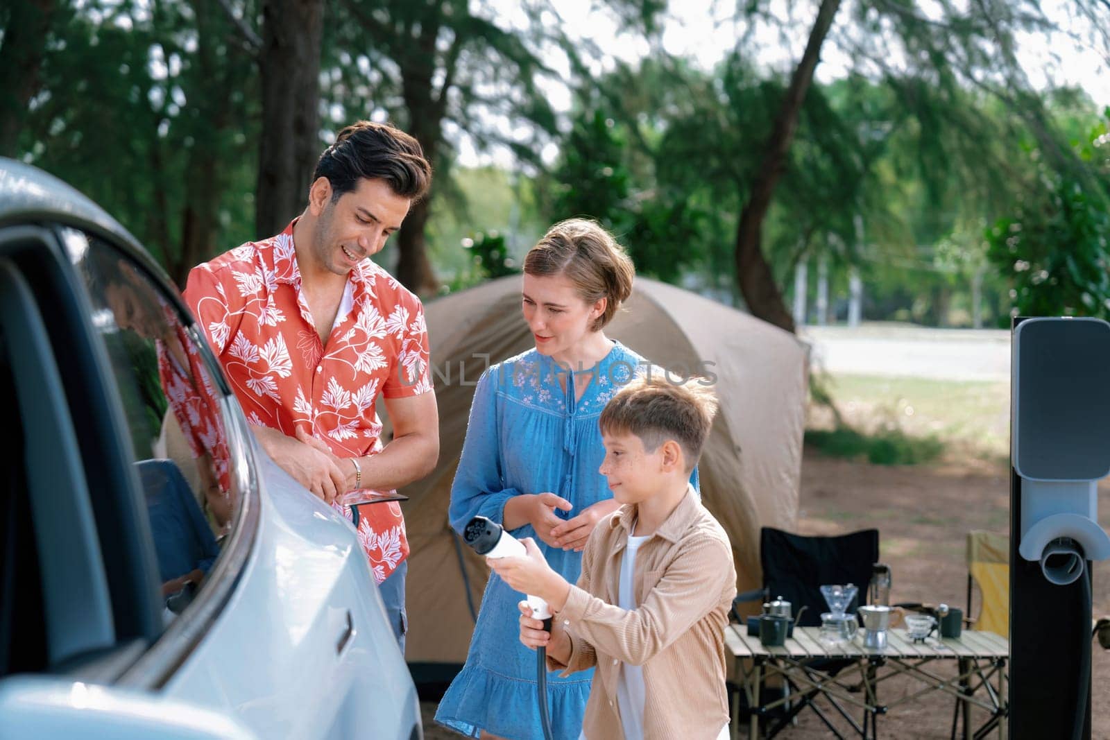 Outdoor adventure and family vacation camping in nature travel by eco friendly car for sustainable future. Lovely family recharge EV car with EV charging station in campsite. Perpetual