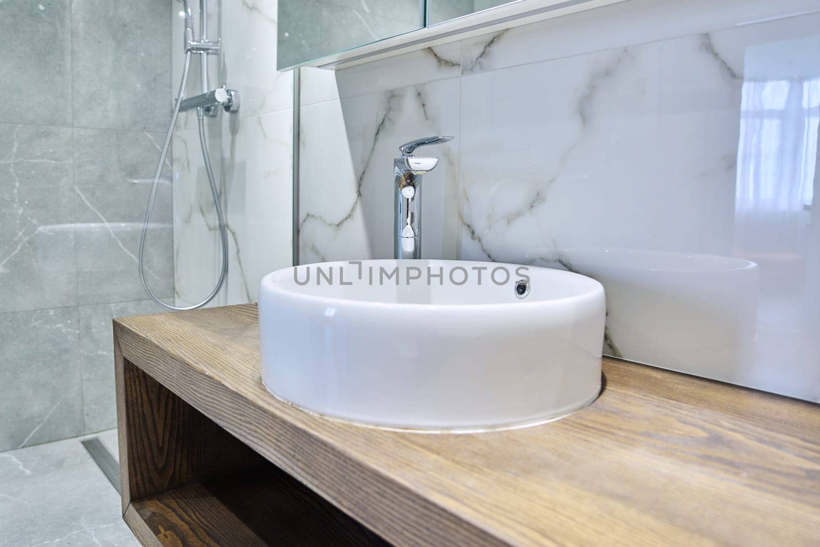 Shower room interior in marble white gray tiles, with countertop round washbasin on wooden bedside table. Modern minimalist style, bathroom cabinet, bathtub.