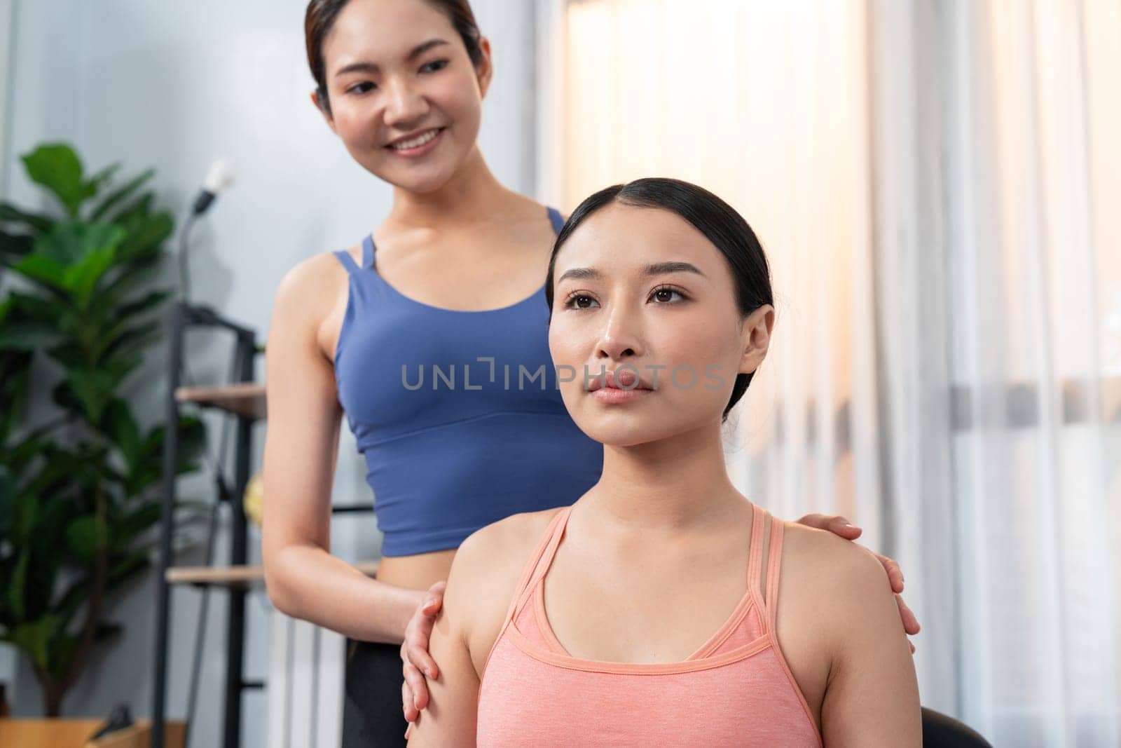 Asian woman in sportswear doing yoga exercise on fitness mat with trainer or workout buddy as home workout training routine. Healthy body care in yoga lifestyle people. Vigorous