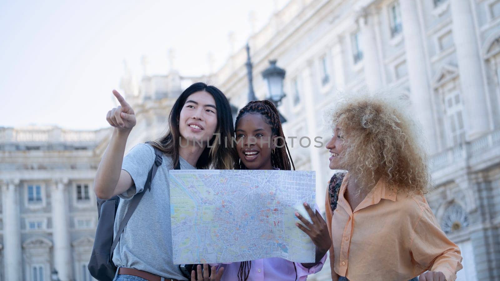 Group of multi ethnic young travellers looking looking and pointing somewhere to visit. A woman is holding a map.