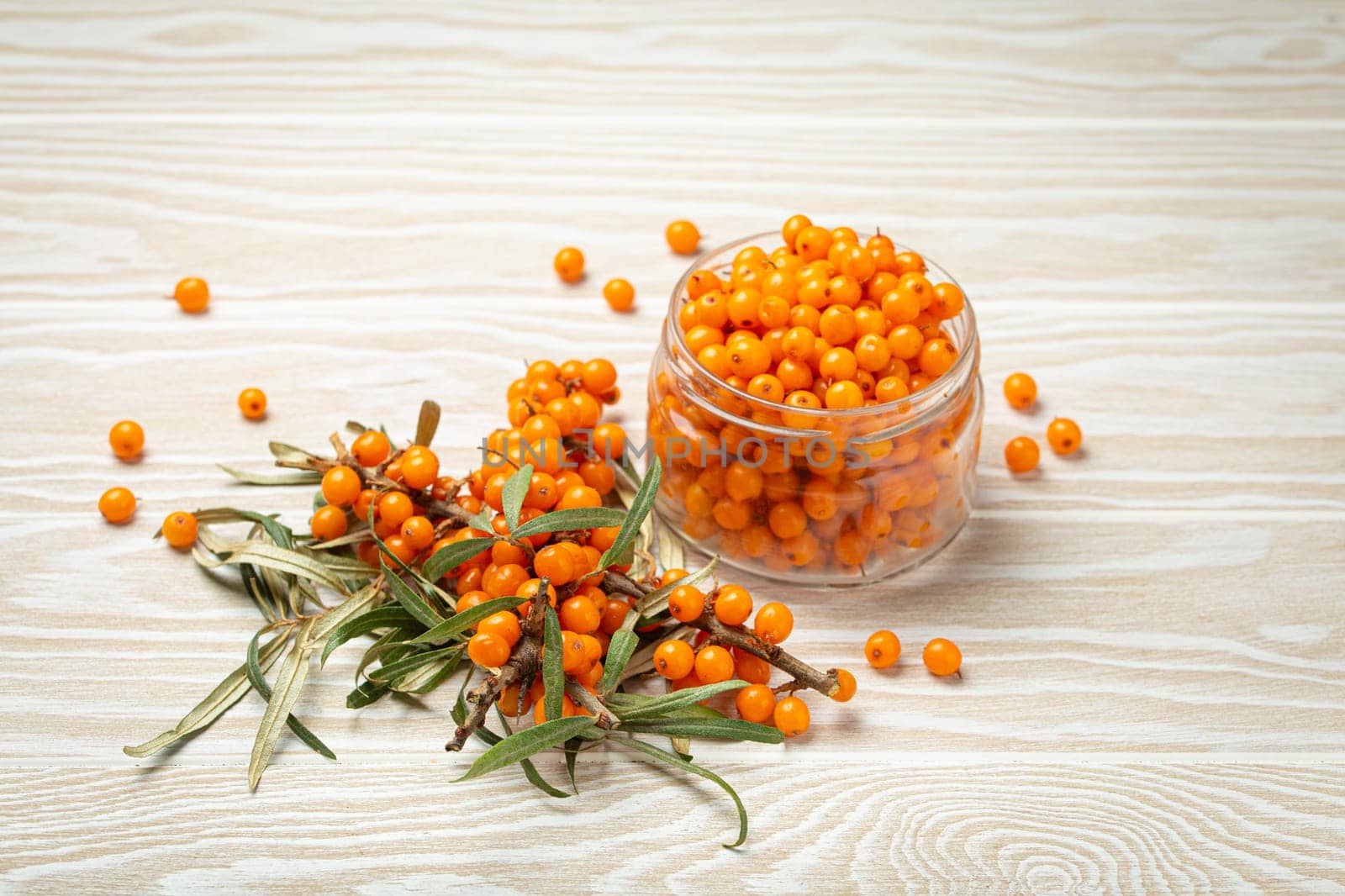 Sea buckthorn ripe berries in glass jar and branches with leaves top view on white wooden rustic background, great for skin, heart, vessels and immune system.
