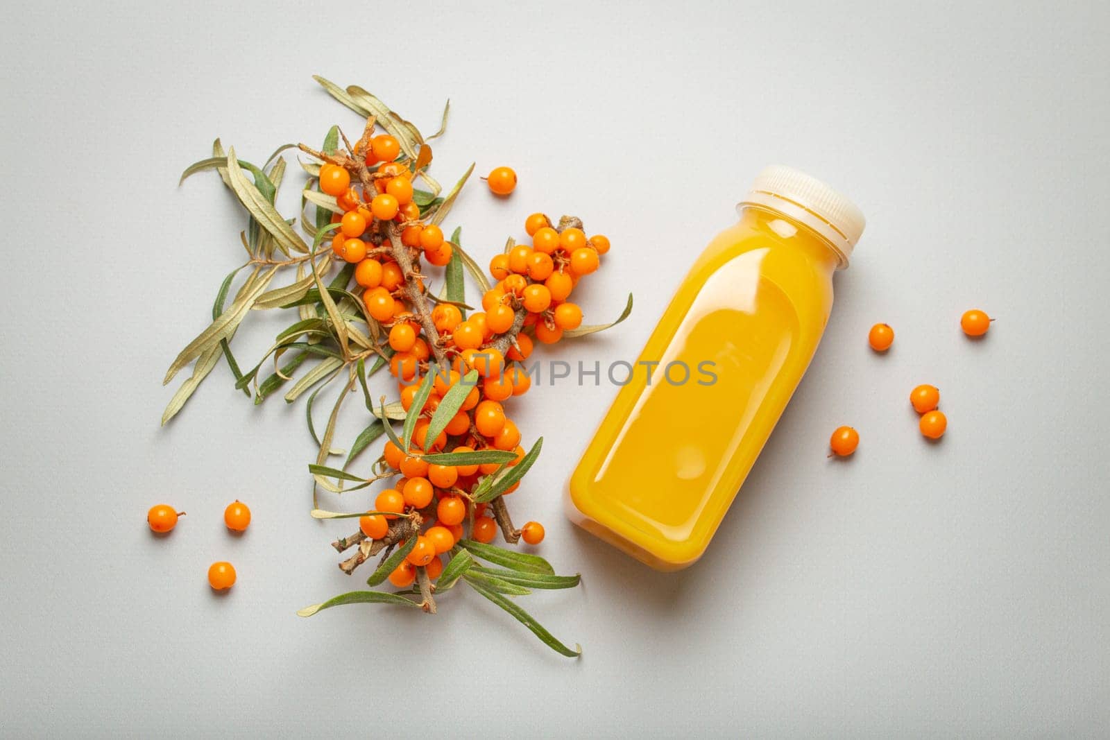 Sea buckthorn healthy juicy drink in bottle and branches with leaves and ripe berries top view on light grey simple background. by its_al_dente