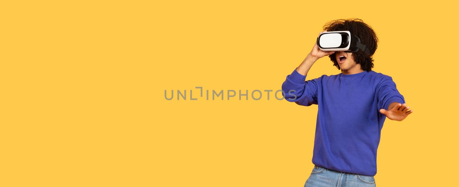 A young black man interacts with virtual reality gear, showcasing excitement in a bright, isolated studio. His casual attire reflects a hipster lifestyle while exploring new digital worlds, copy space