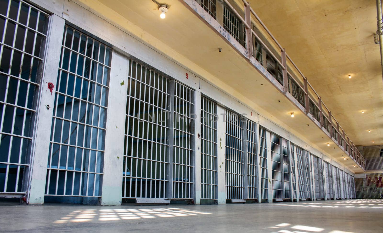 A prison cell block with many cells and bars. The bars are very tall and the windows are small