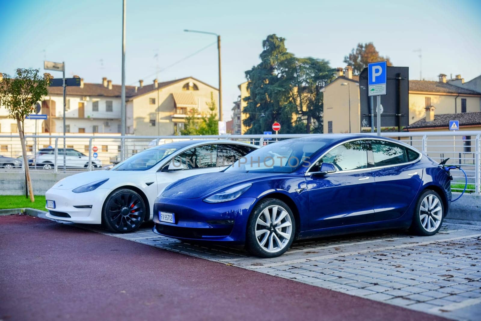 Cremona, Itally - October 6th 2024 Two tesla model 3 electric cars, one in blue and one in white, parked in a designated charging area