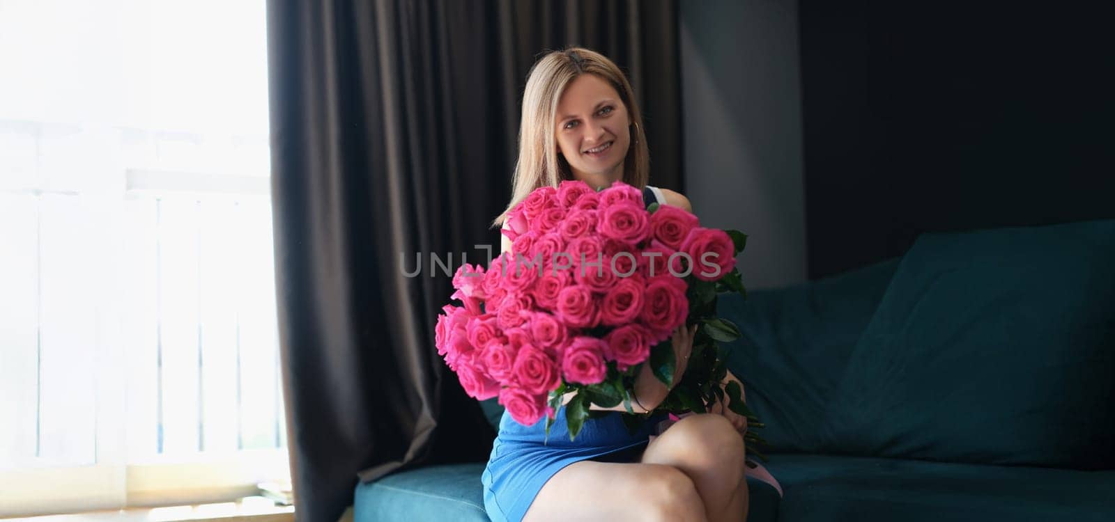 A young woman is sitting on a sofa with a large bouquet of roses, close-up. Romance, holiday greetings, wedding anniversary