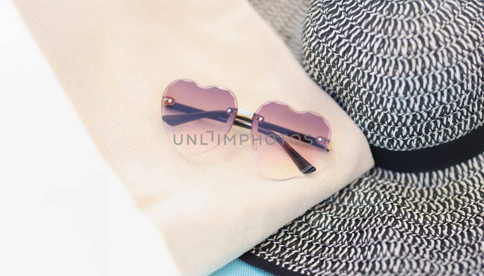 Sunglasses and a straw hat lie on a towel, close-up. Beach accessories, sun protection, vintage style