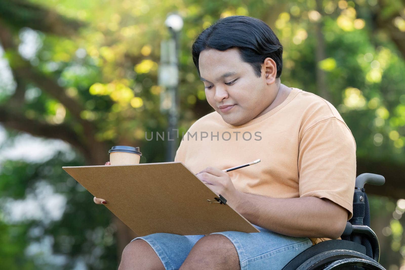 A young artist in a wheelchair sketches in a park, enjoying a sunny day with a coffee cup nearby.