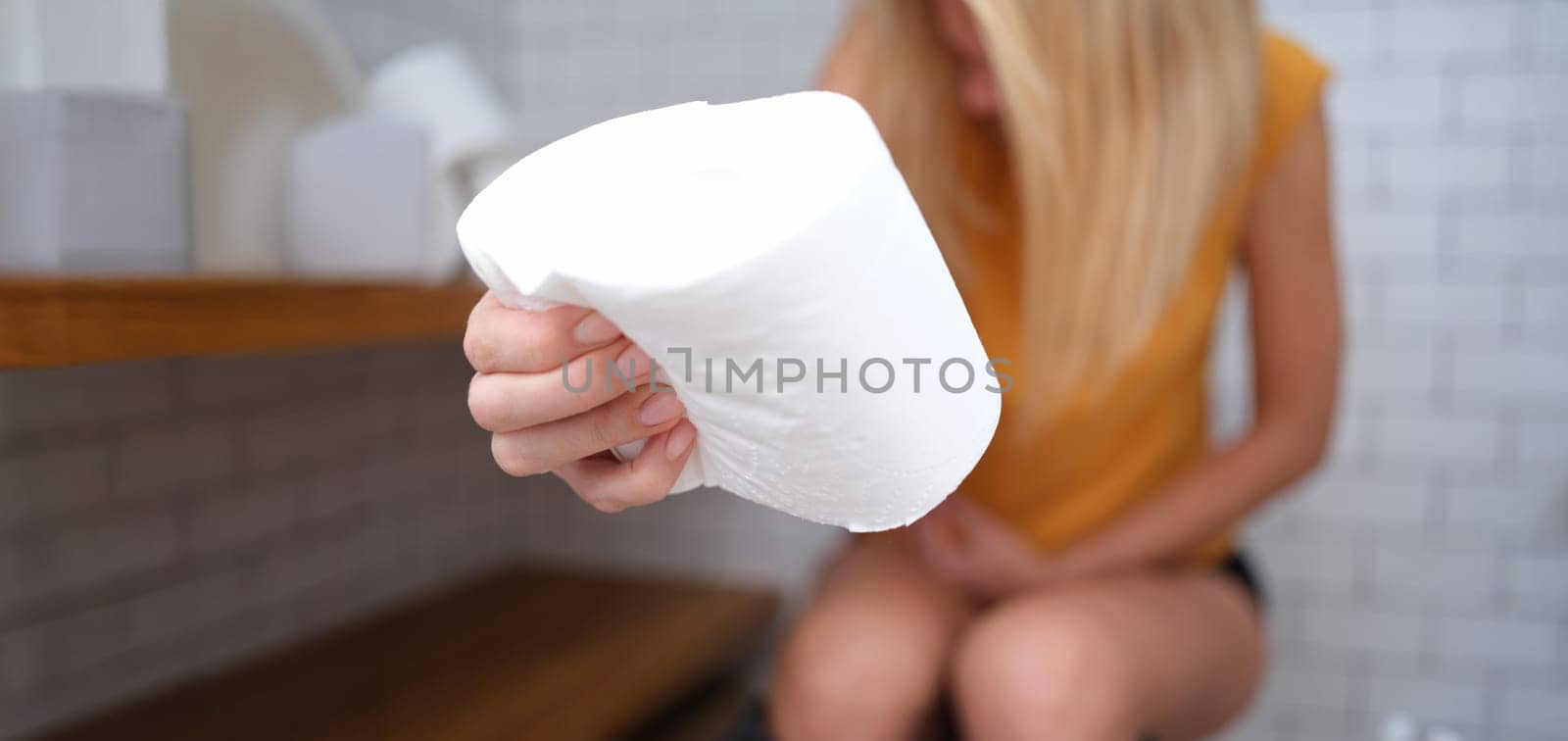 A woman is sitting on the toilet with toilet paper in her hand, close-up, blurry. Abdominal pain, diarrhea, constipation