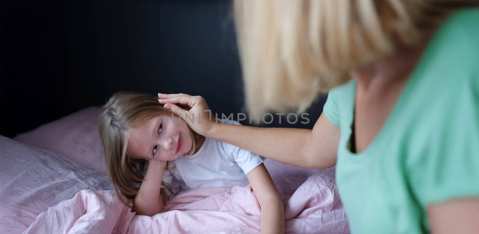 Mom strokes the child on the head, close-up. The daughter sits on the bed, the woman calms the girl