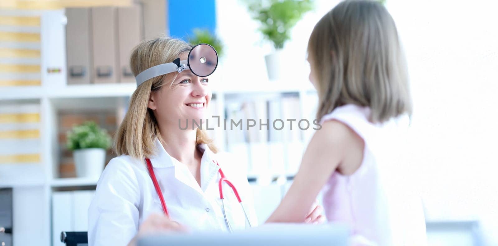 Female doctor at the clinic smiling at the little girl. Children's otolaryngologist, diagnostics of throat diseases