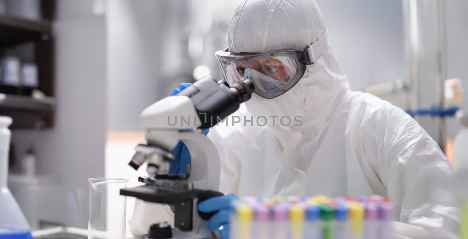 A man in a protective uniform looks through an X-ray microscope, close-up. Laboratory equipment, quality assessment