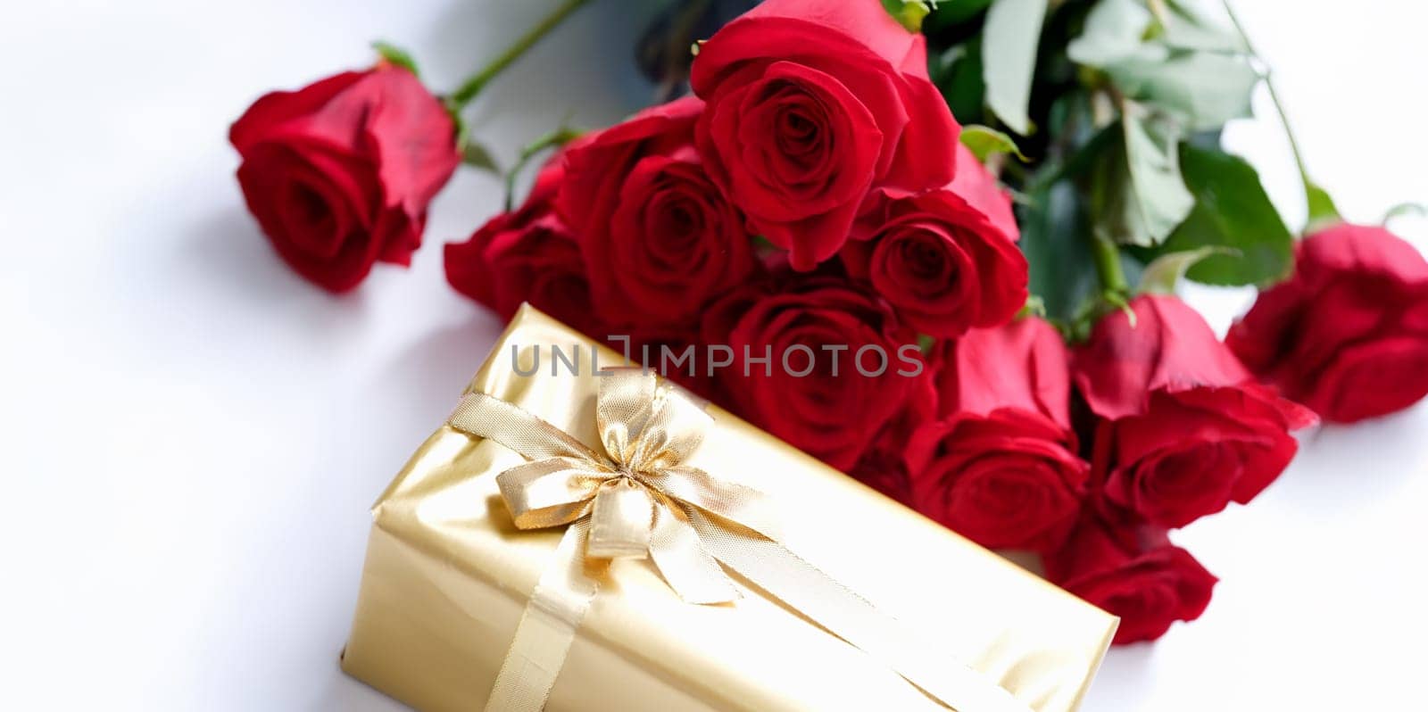 Gift wrapped in gold and a bouquet of red roses, close-up. Beautiful fighting box with ribbon, floristry