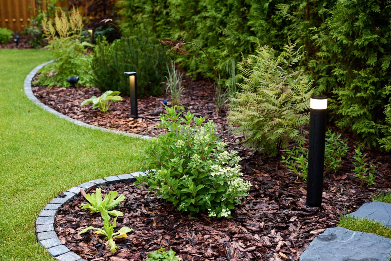 A beautifully serene garden featuring vibrant greenery, elegant twinkling lights, and decorative mulch pathways