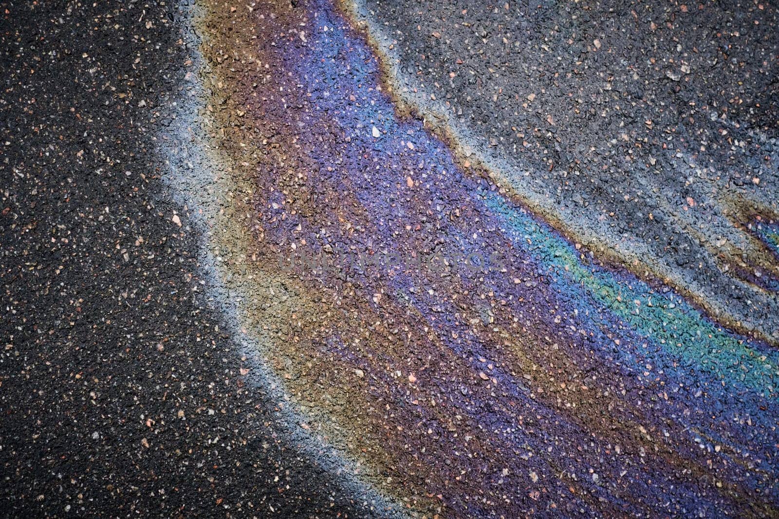 Rainbow oil stain on asphalt driveway surface showing spectrum of colors