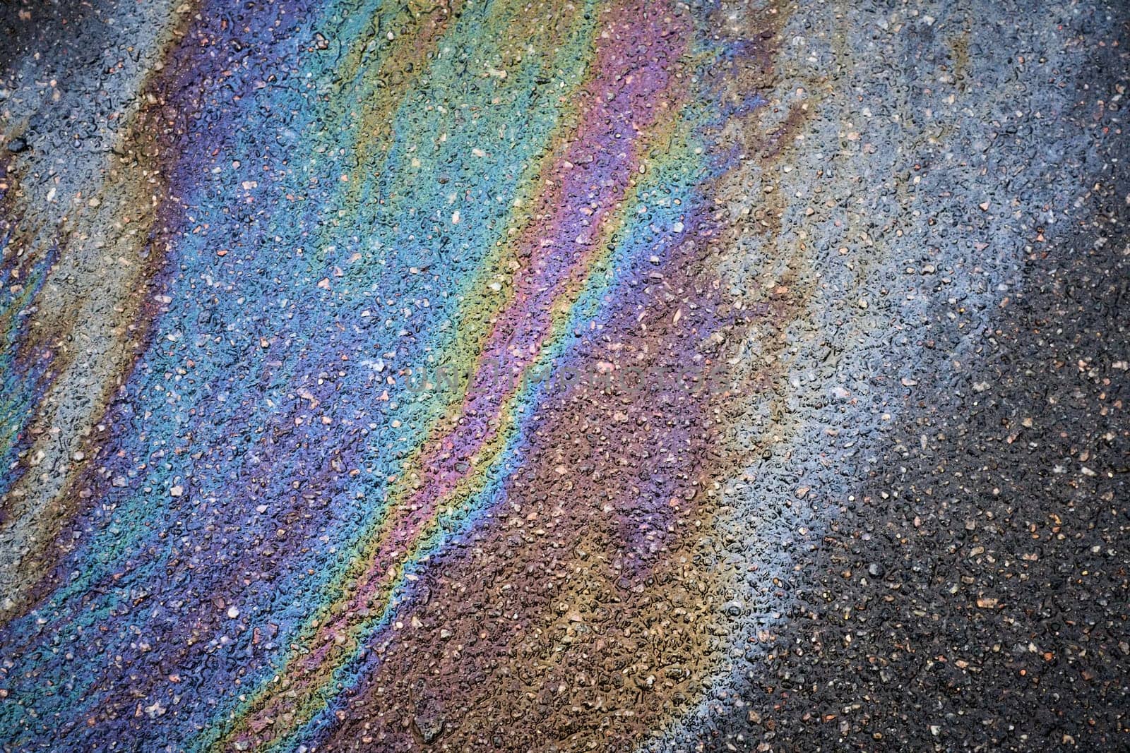 Gasoline or oil spill on asphalt creating rainbow pattern. Colorful gasoline or oil spill creating a rainbow pattern on asphalt, indicating pollution and environmental damage.