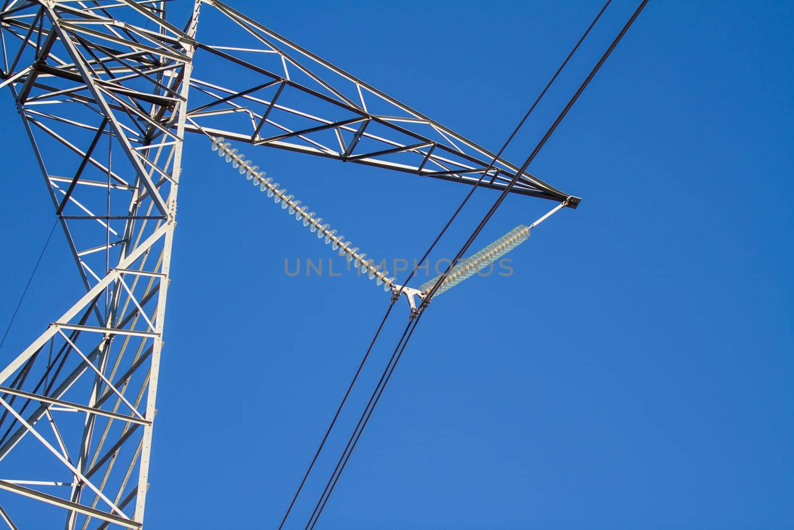 A tall power line tower with a blue sky in the background. The sky is clear and bright, and the tower is the main focus of the image