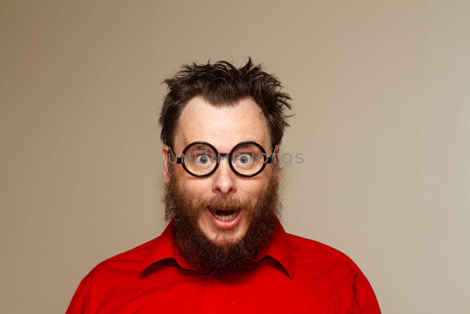 A man with glasses and a beard is smiling and looking surprised. He is wearing a red shirt