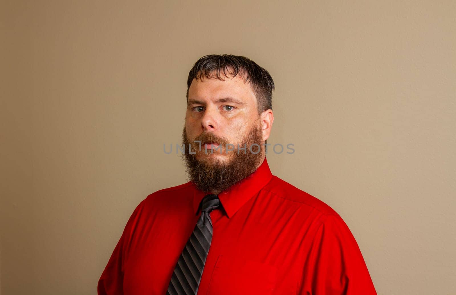 A man with a beard and a red shirt and a black tie.
