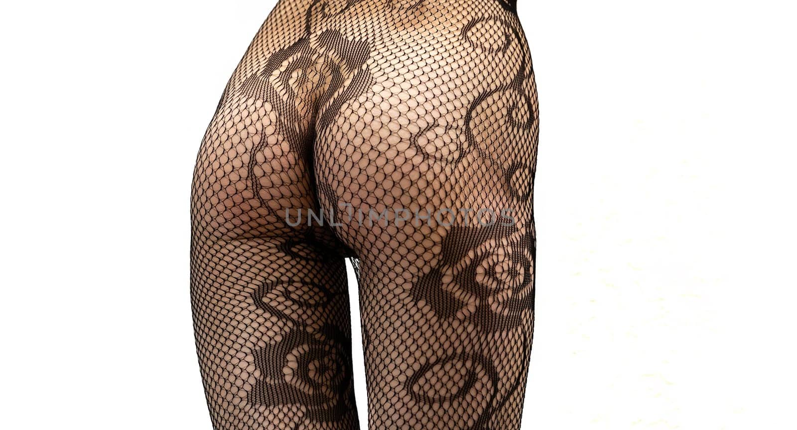 A young woman poses confidently against a plain white background, wearing only fishnet tights. Her body highlights a slim and alluring figure, emphasizing curves and elegance.