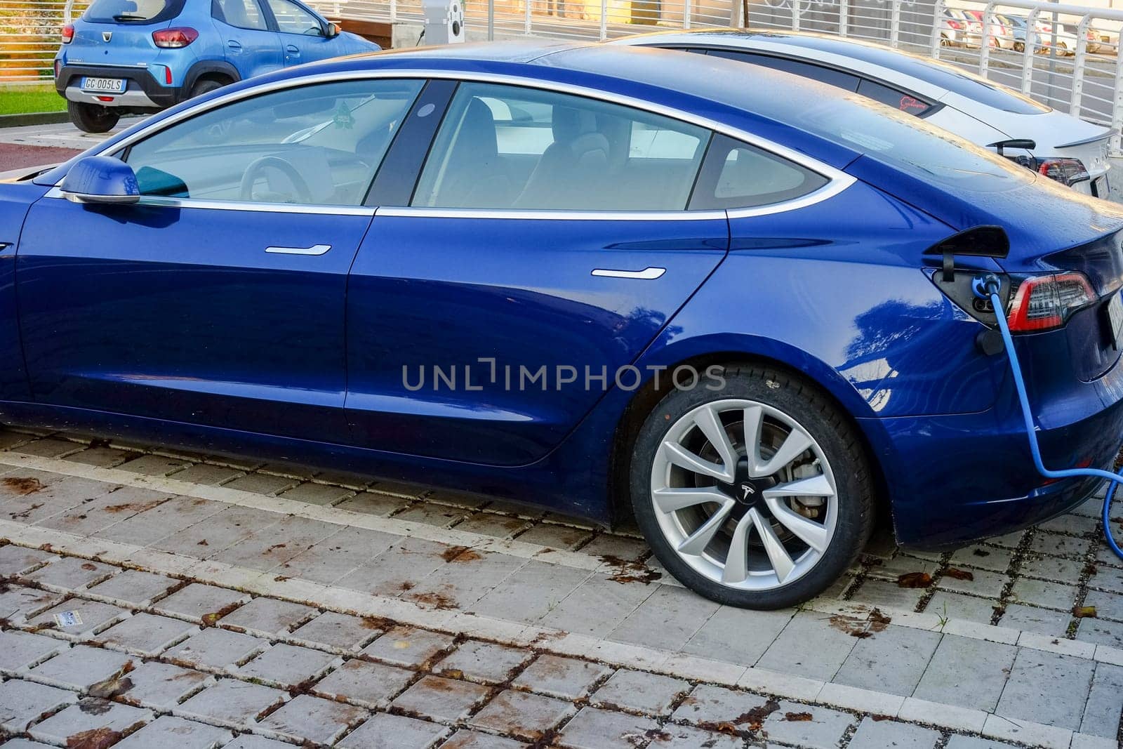 Cremona, Itally - October 6th 2024 Deep blue metallic tesla model 3 long range with dual motor all-wheel drive charging its battery at a charging station