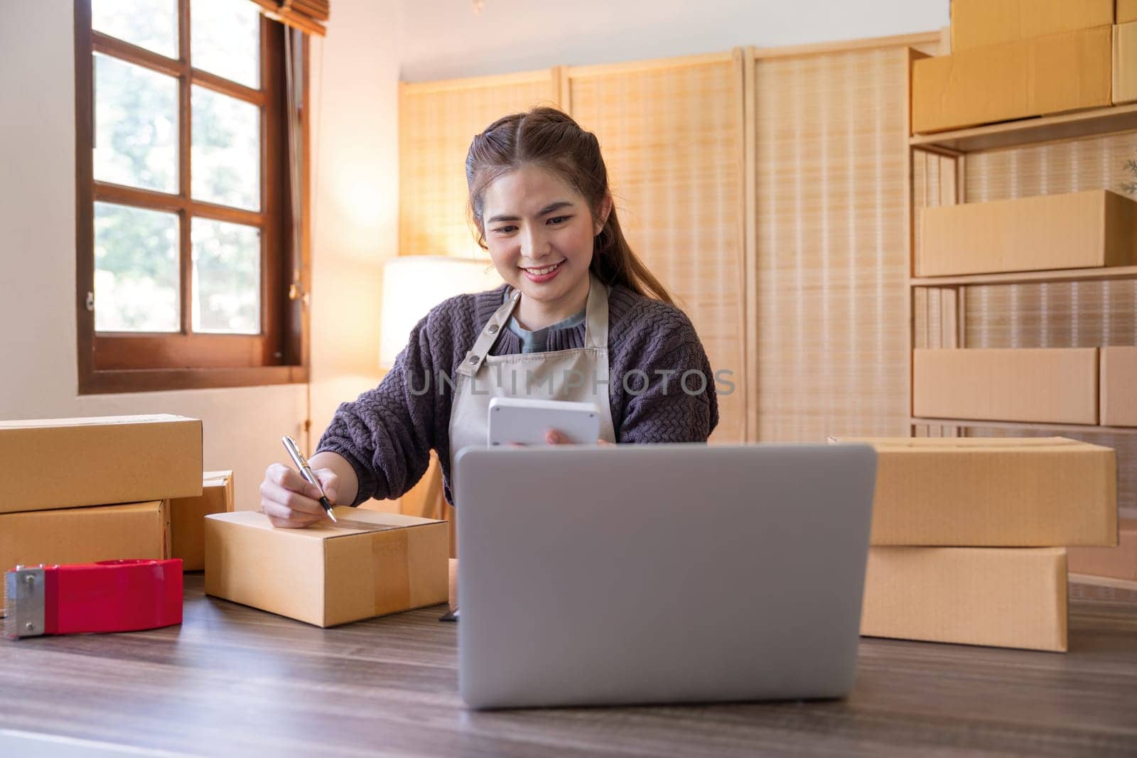 Woman asian is writing a list of customer on paper before shipping to them, she runs an ecommerce business on websites and social media. Concept of selling products online.