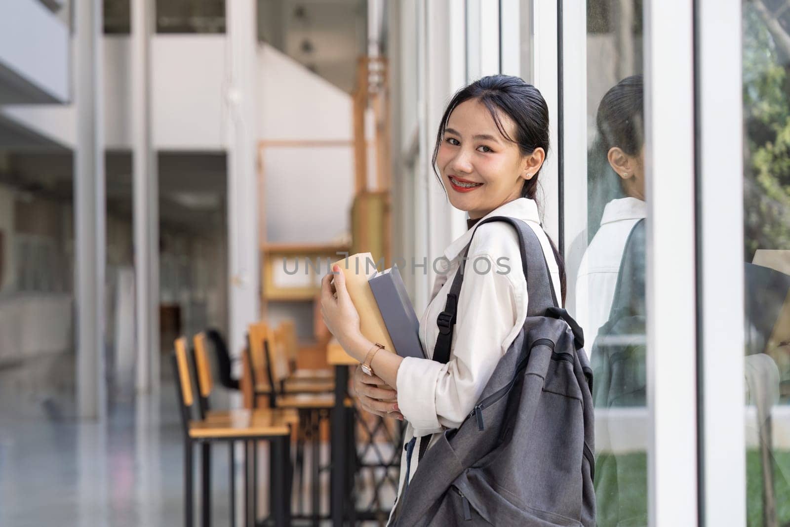 Beautiful young woman asian with backpack and book. College student carrying lots of books in college campus.