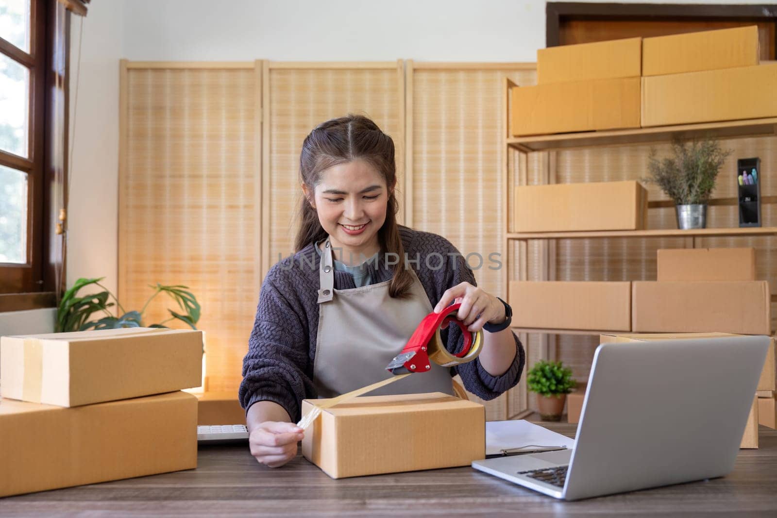Woman asian use scotch tape to attach parcel boxes to prepare goods for the process of packaging, shipping, online sale internet marketing ecommerce concept startup business idea.