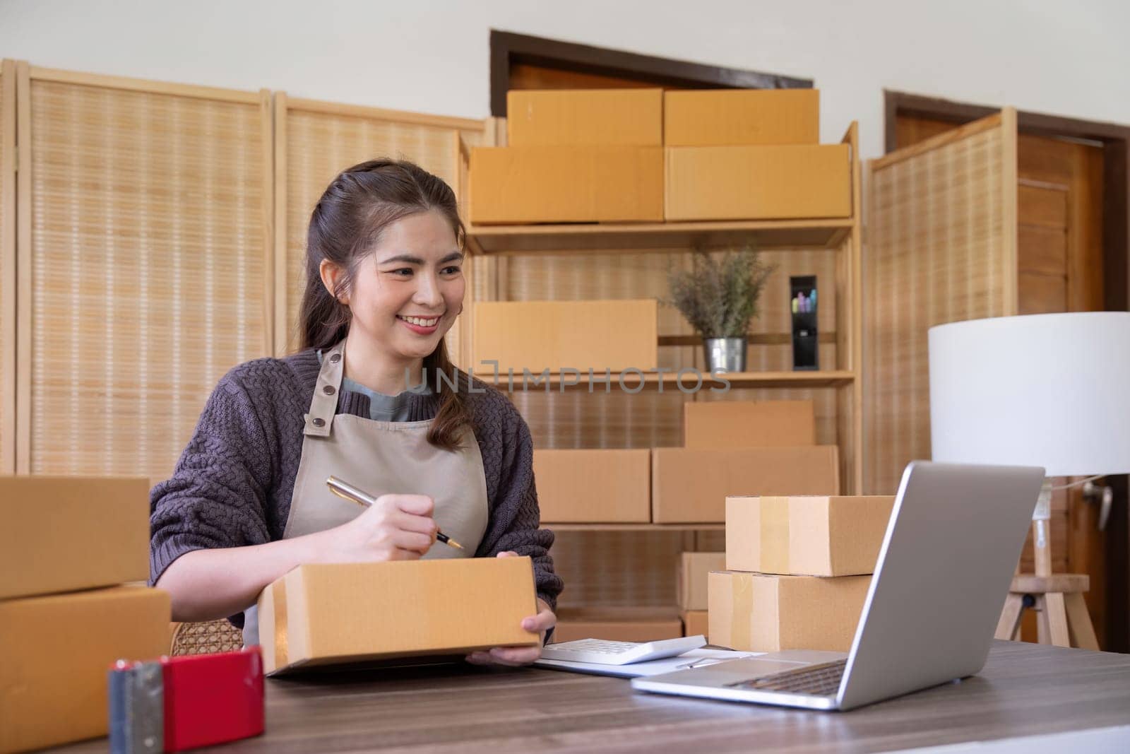 Woman asian is writing a list of customer on paper before shipping to them, she runs an ecommerce business on websites and social media. Concept of selling products online.