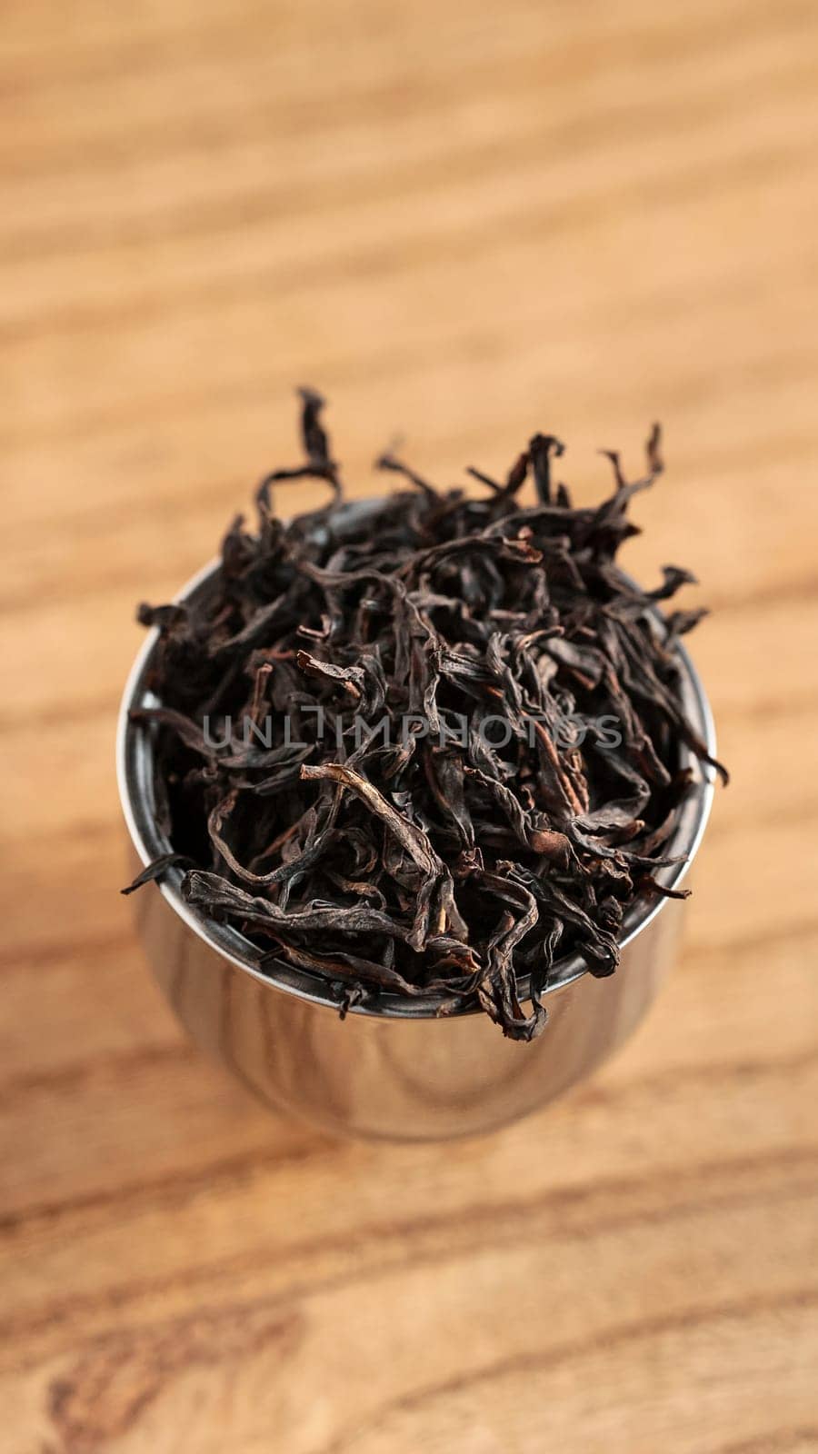 A closeup view of dried black tea leaves being held in a metal scoop placed on a rustic wooden background