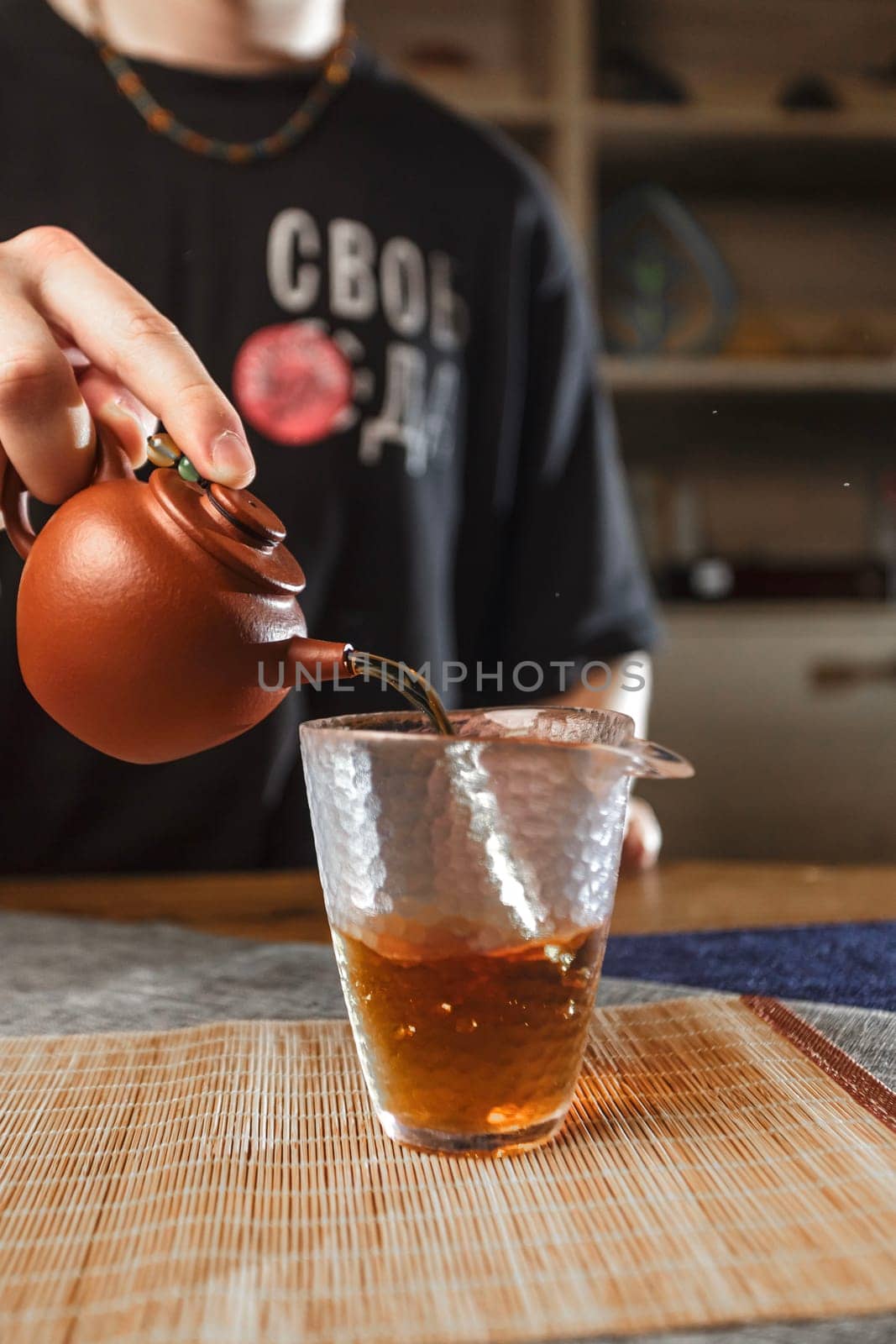 A closeup of tea being poured from a crafted teapot into a delicate glass cup, showcasing a cozy tea moment
