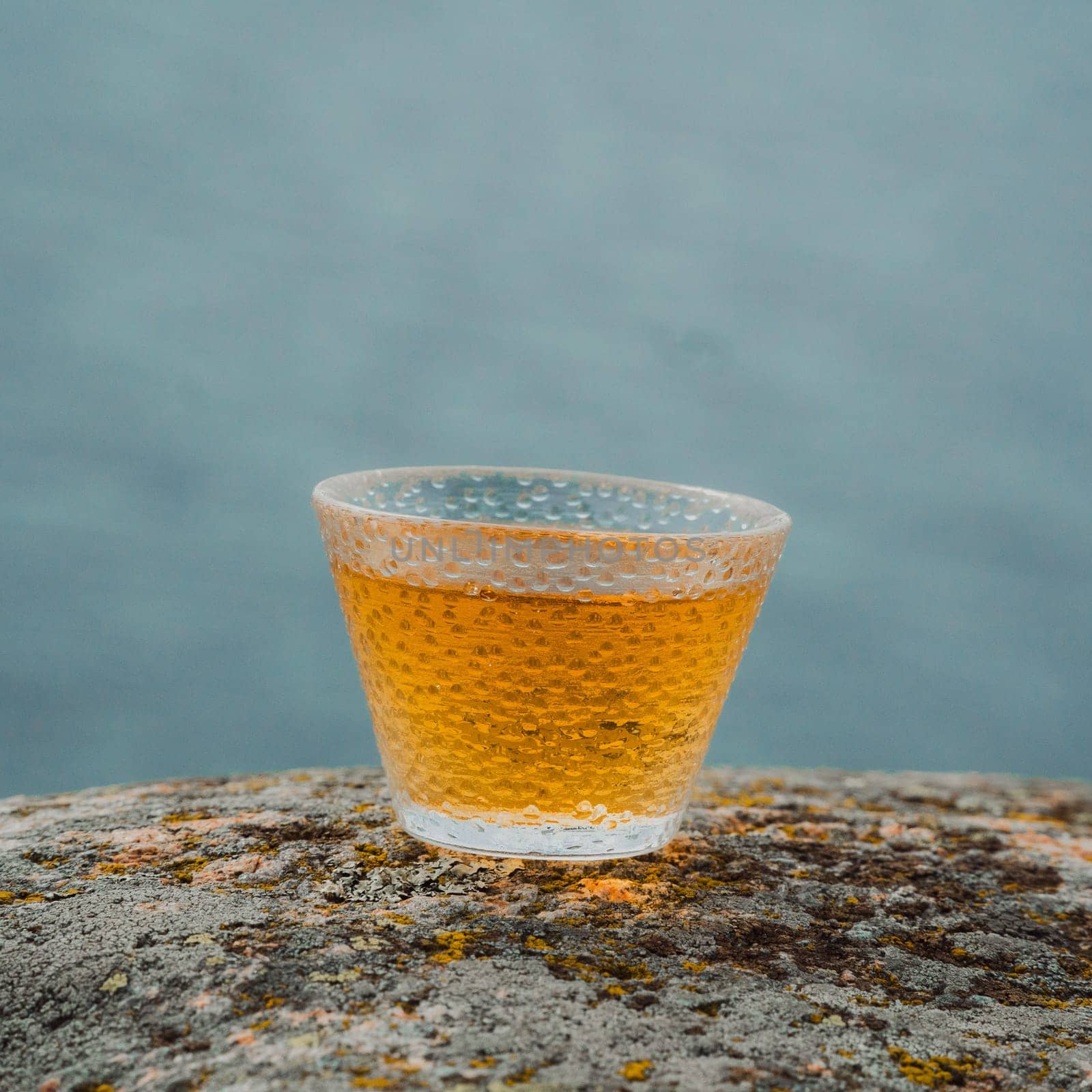 A closeup view of a beautifully filled, textured glass cup elegantly placed on a rugged stone surface