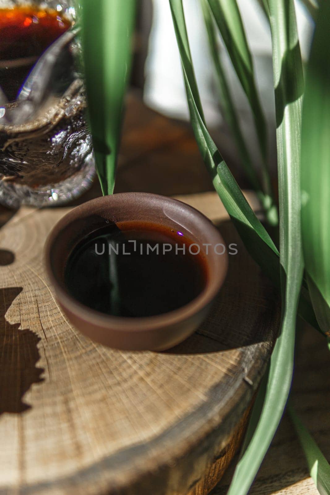 A beautiful view shows dark syrup in a clay bowl, surrounded by greenery and textures, creating a captivating scene