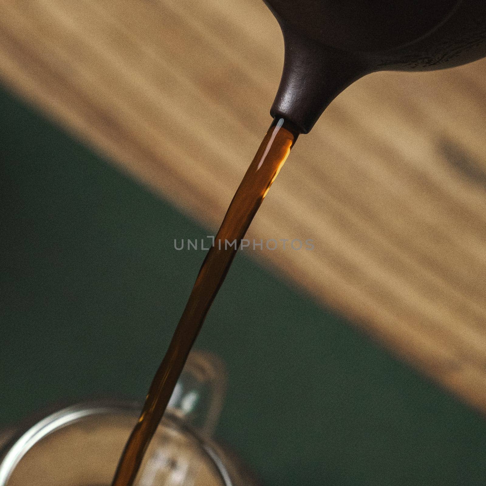 A closeup shot capturing the rich, dark brown coffee being elegantly poured from a kettle into a glass mug