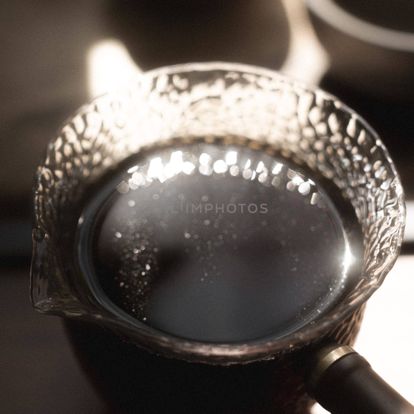 A closeup view of a beautifully decorative teapot filled with rich dark liquid, capturing elegant reflections of light