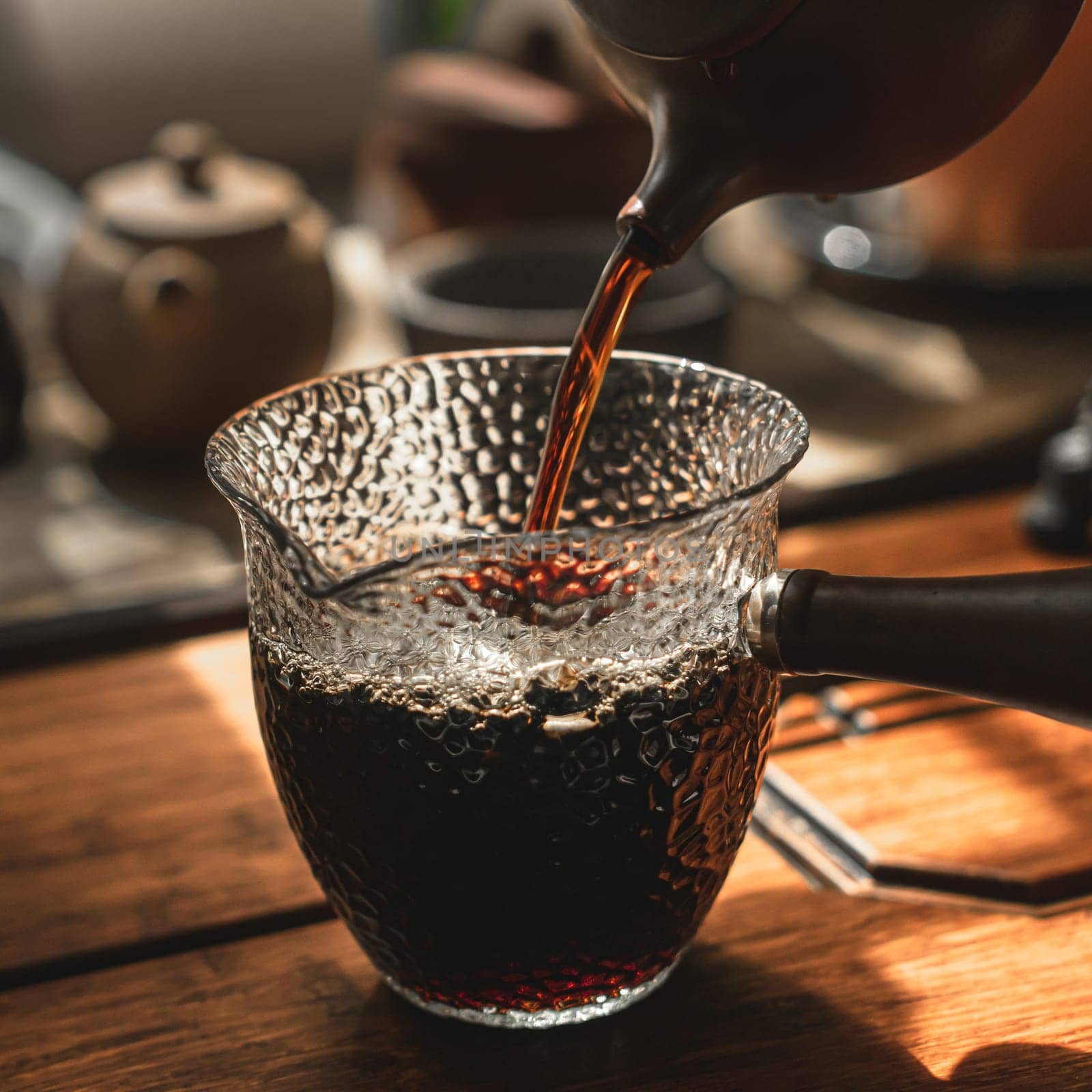 Coffee is elegantly poured from a pot into a textured glass carafe, enhancing a warm and inviting ambiance