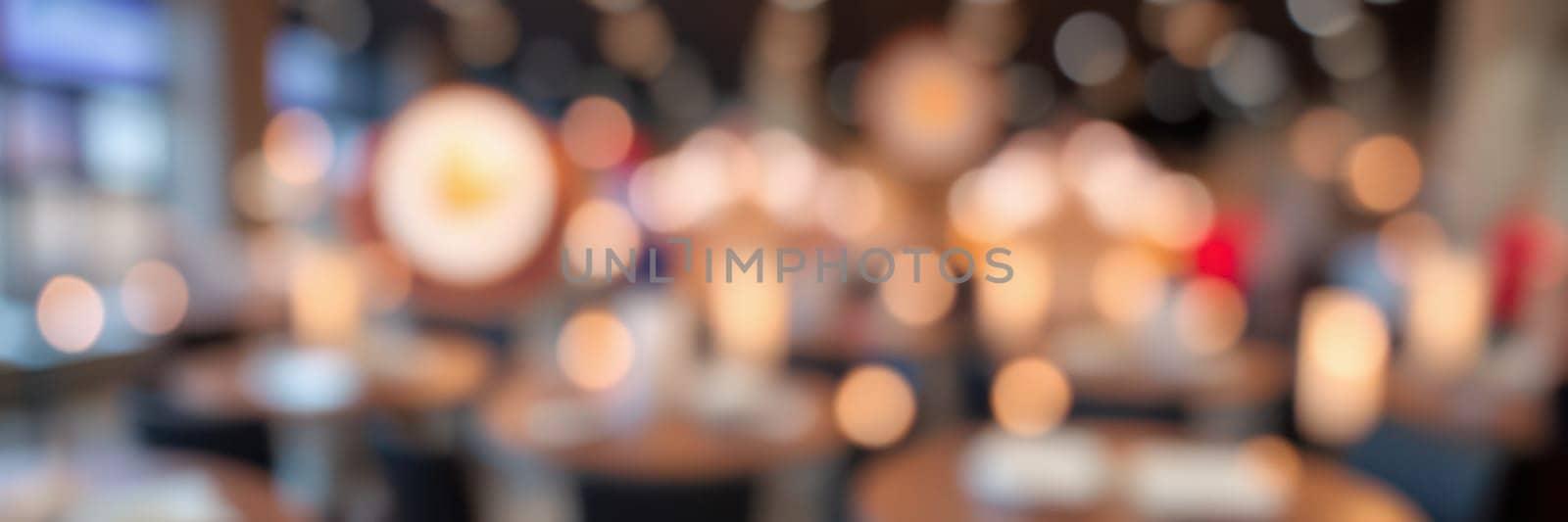 A bustling dining space showcases round tables and chairs set for guests. Warm lights create an inviting ambiance, enhancing the lively atmosphere of a popular restaurant in the evening.