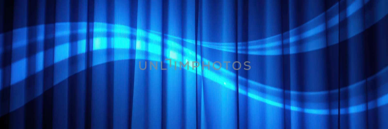 A bright blue stage curtain hangs in a theater, illuminated with soft lighting. Wave patterns enhance the dramatic atmosphere, setting the stage for the upcoming performance.