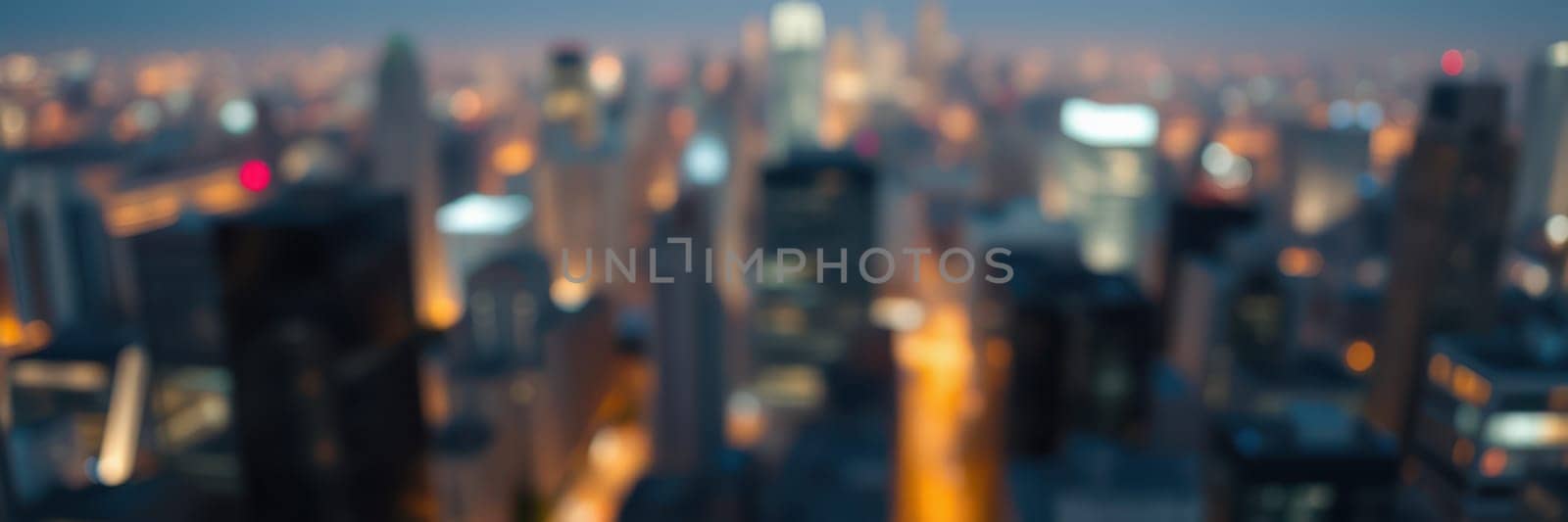 The urban skyline features skyscrapers glowing with lights in a bustling city during nighttime. The blurred image captures the lively atmosphere and energy of the metropolis.