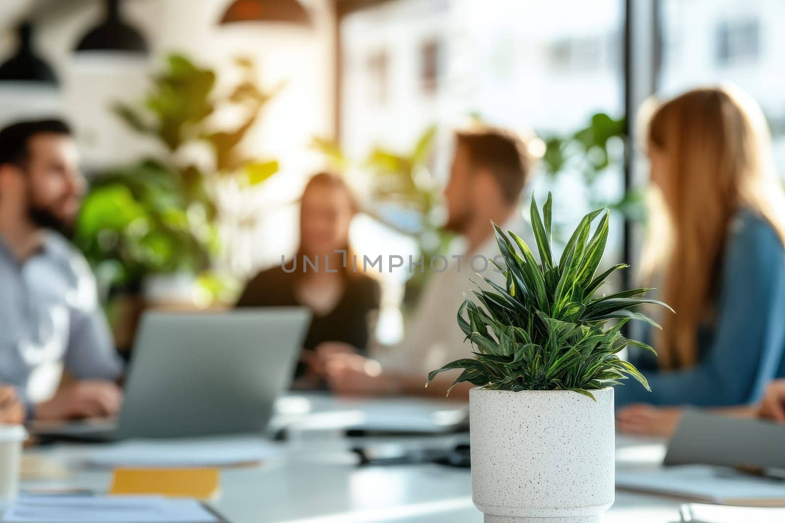 A vibrant office scene showcases professionals engaged in discussion around a table with plants. Laptops and documents illustrate a creative teamwork environment.