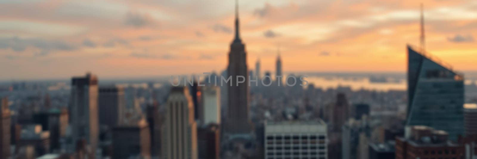 A stunning sunset illuminates the New York City skyline, highlighting famous structures like the Empire State Building amidst a vast urban landscape. The warm colors create a serene atmosphere.