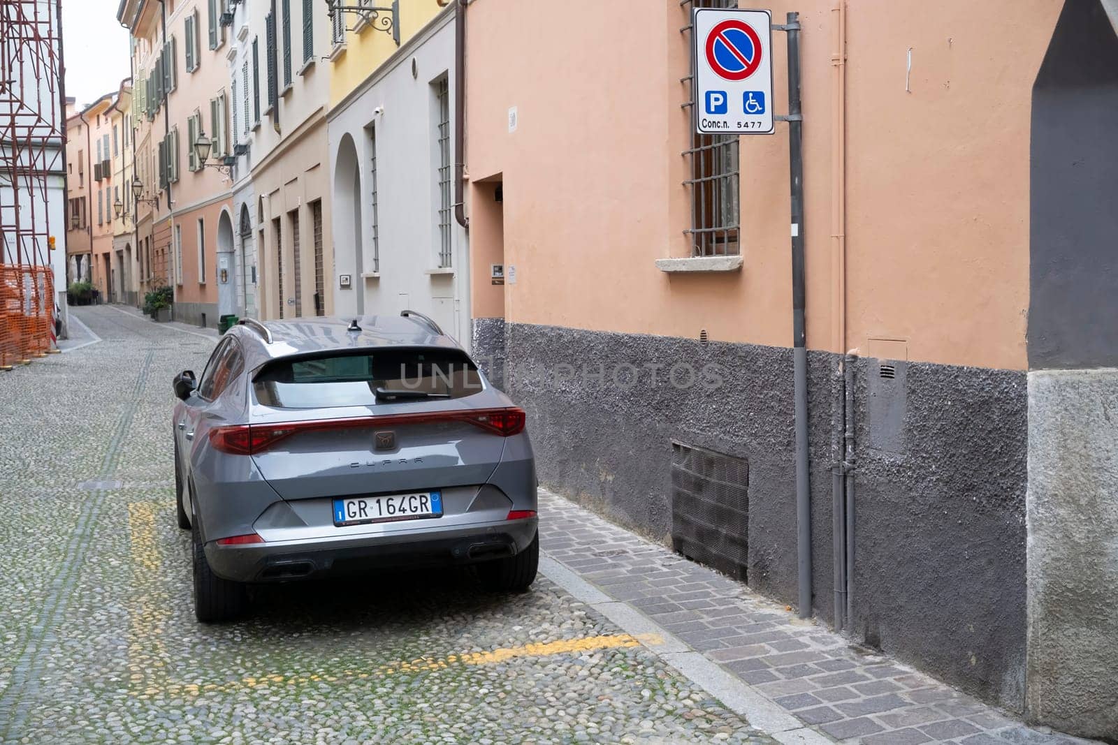 Lombardy, Italy - November 20th 2024 Rear view of a grey cupra formentor parked in a no parking or stopping area reserved for disabled people in a narrow cobblestone street of an italian town