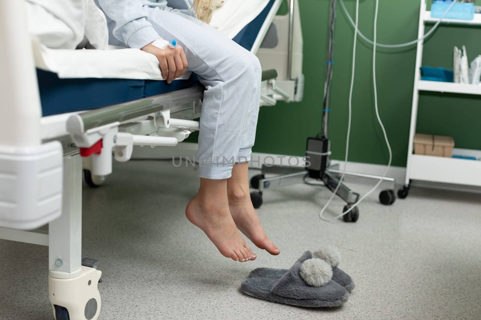 A patient is comfortably sitting on a hospital bed, wearing soft pajamas, with cozy slippers placed on the floor
